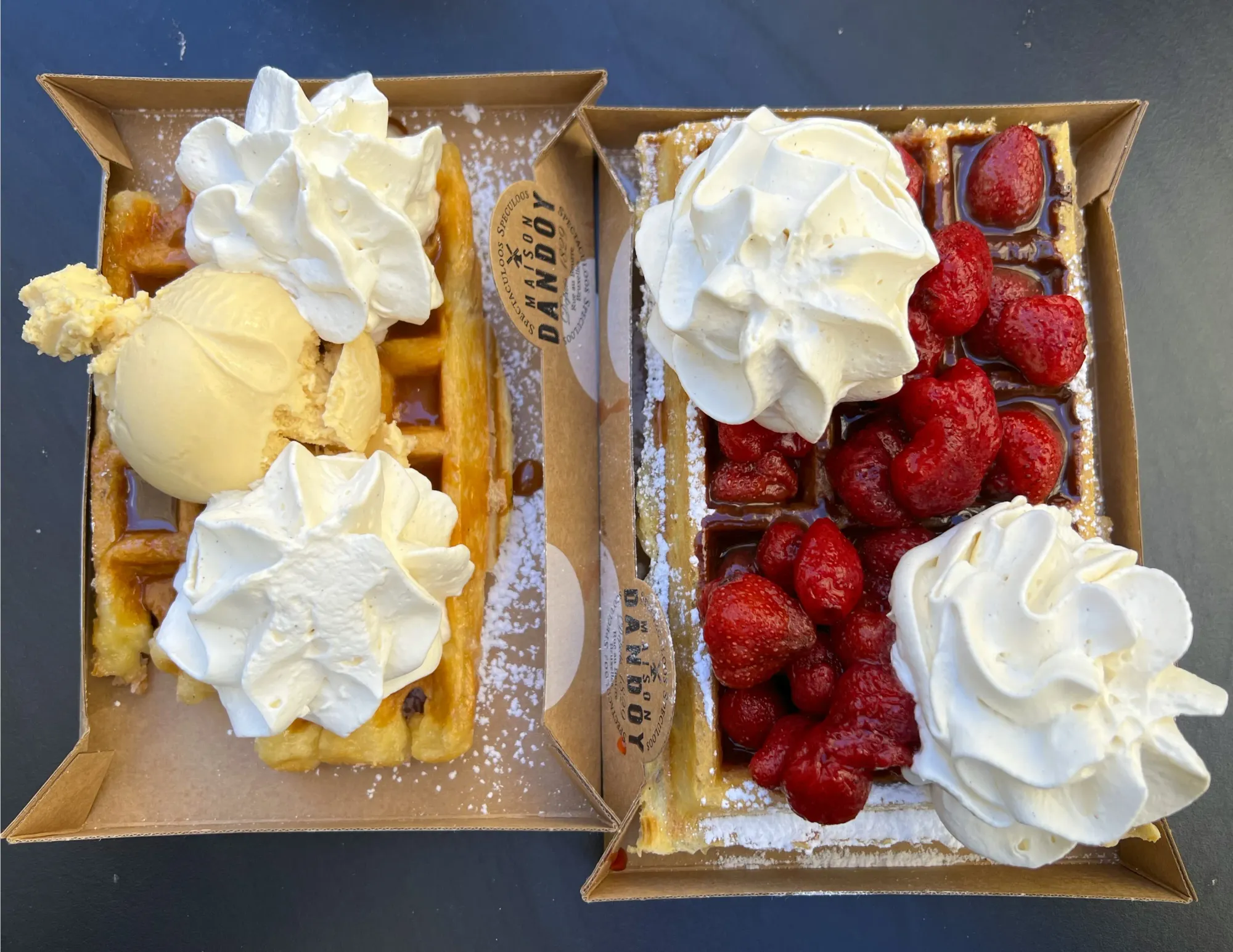 Two waffles one with ice cream the other with berries, both covered in whipped cream