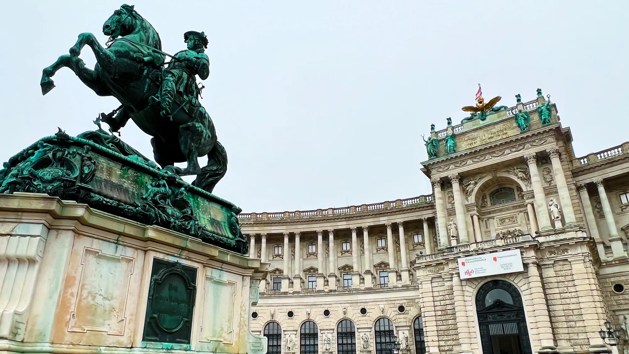 Stone building with a green statue of a mounted horse in the foreground.