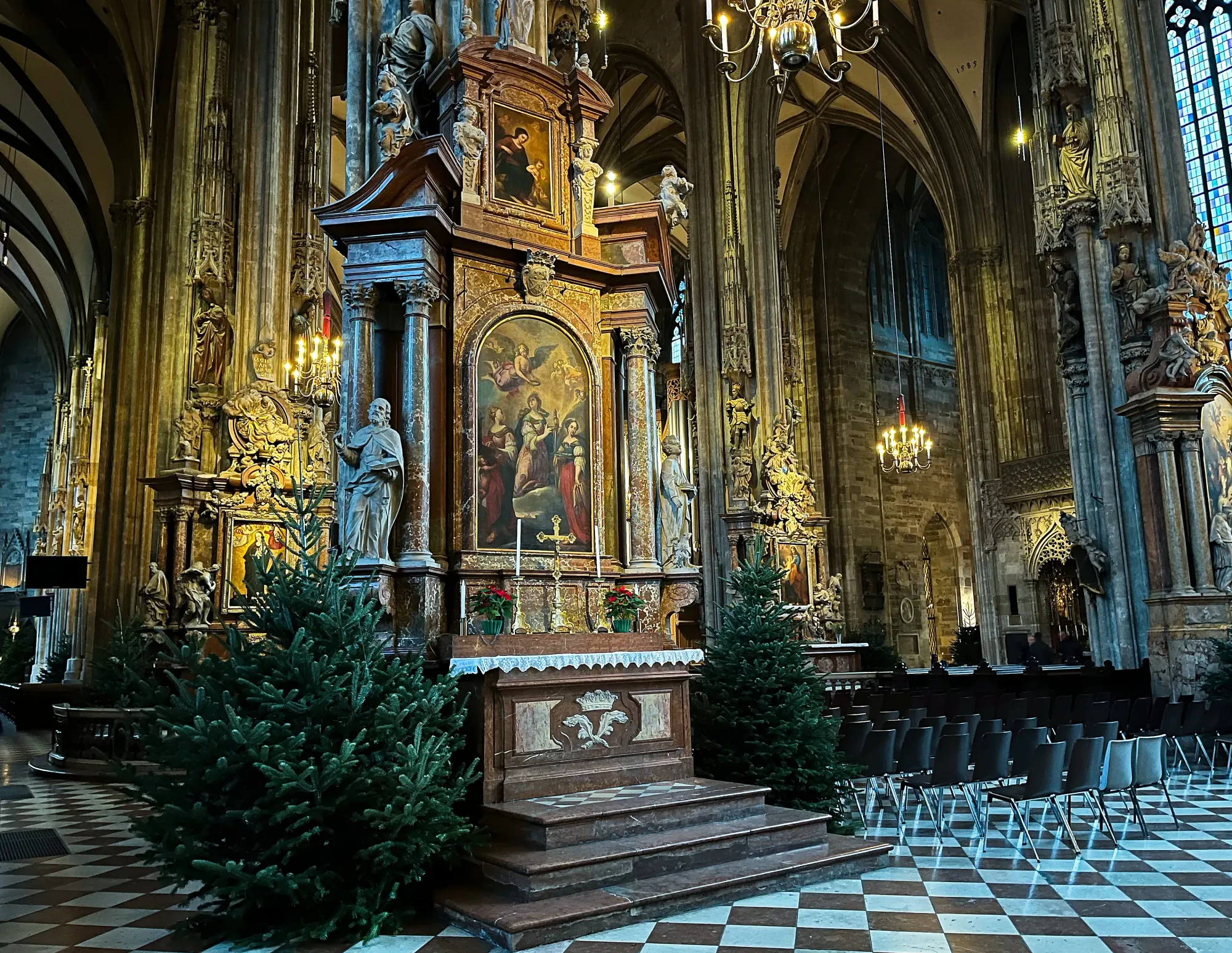 Inside of the church with black and white tiled floors, christmas trees for decoration, and ornately decorated columns