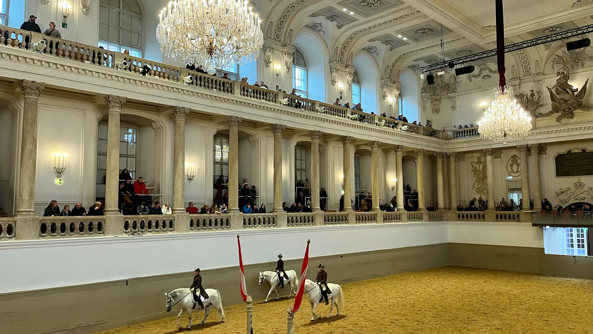 White columned seating with horses being ridden in the middle