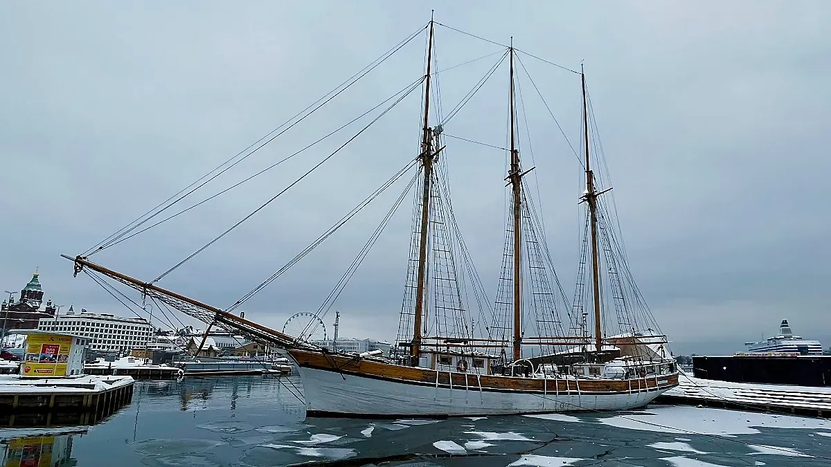 Wooden boat, painted white, floating over sheets of ice in a cloudy harbor