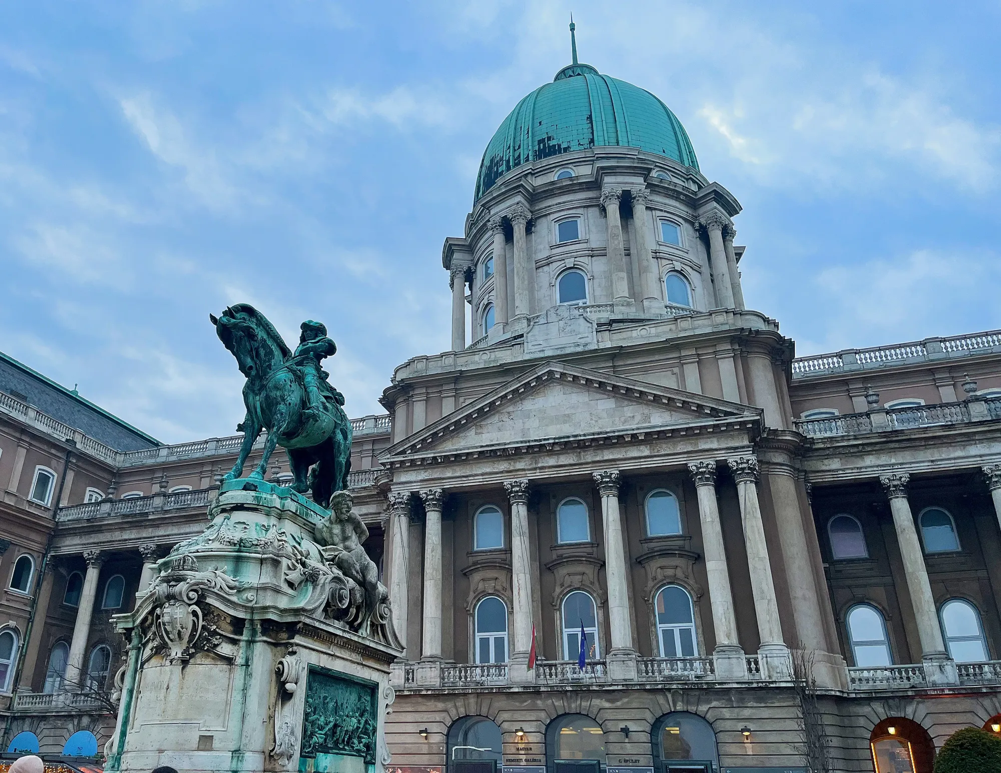 Columned facade with green dome and a green horse and rider statue in front of it