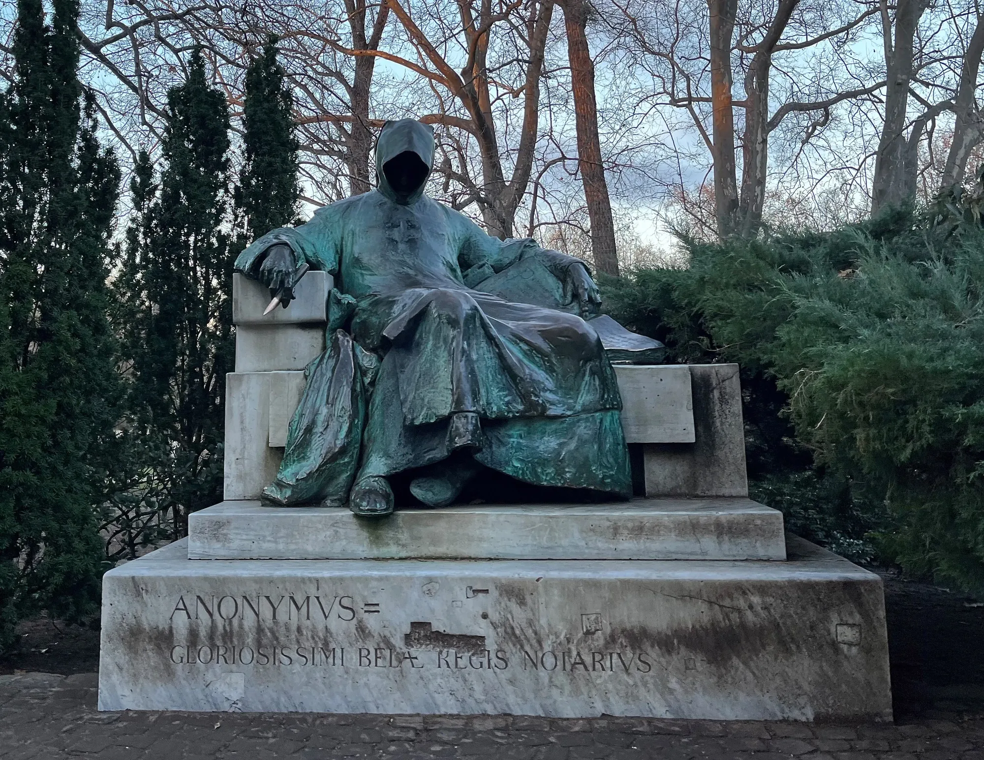 Eerie green statue reclining in a throne with a pen and notebook, and a hood covering their face