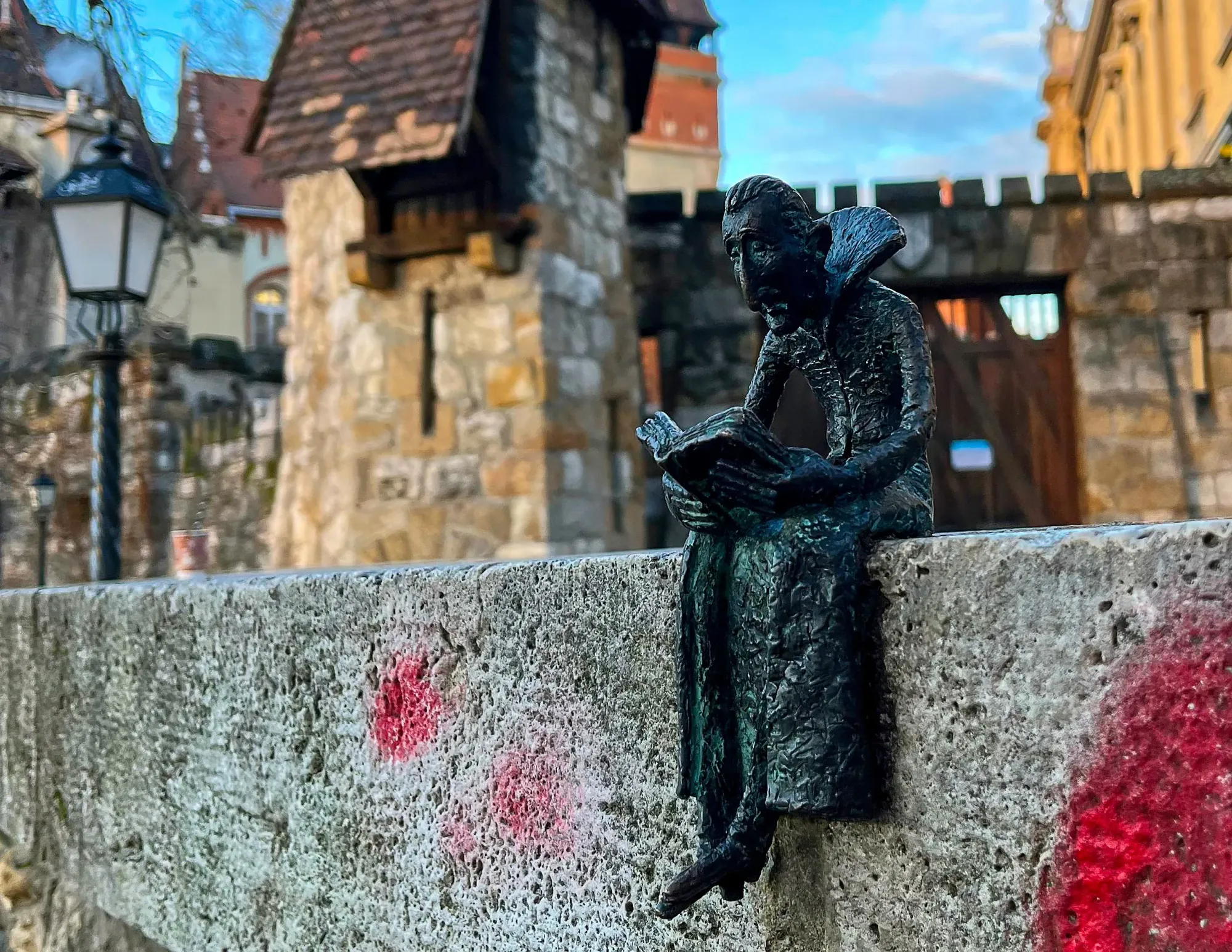 Black statue of Dracula reading a book while sitting on a ledge