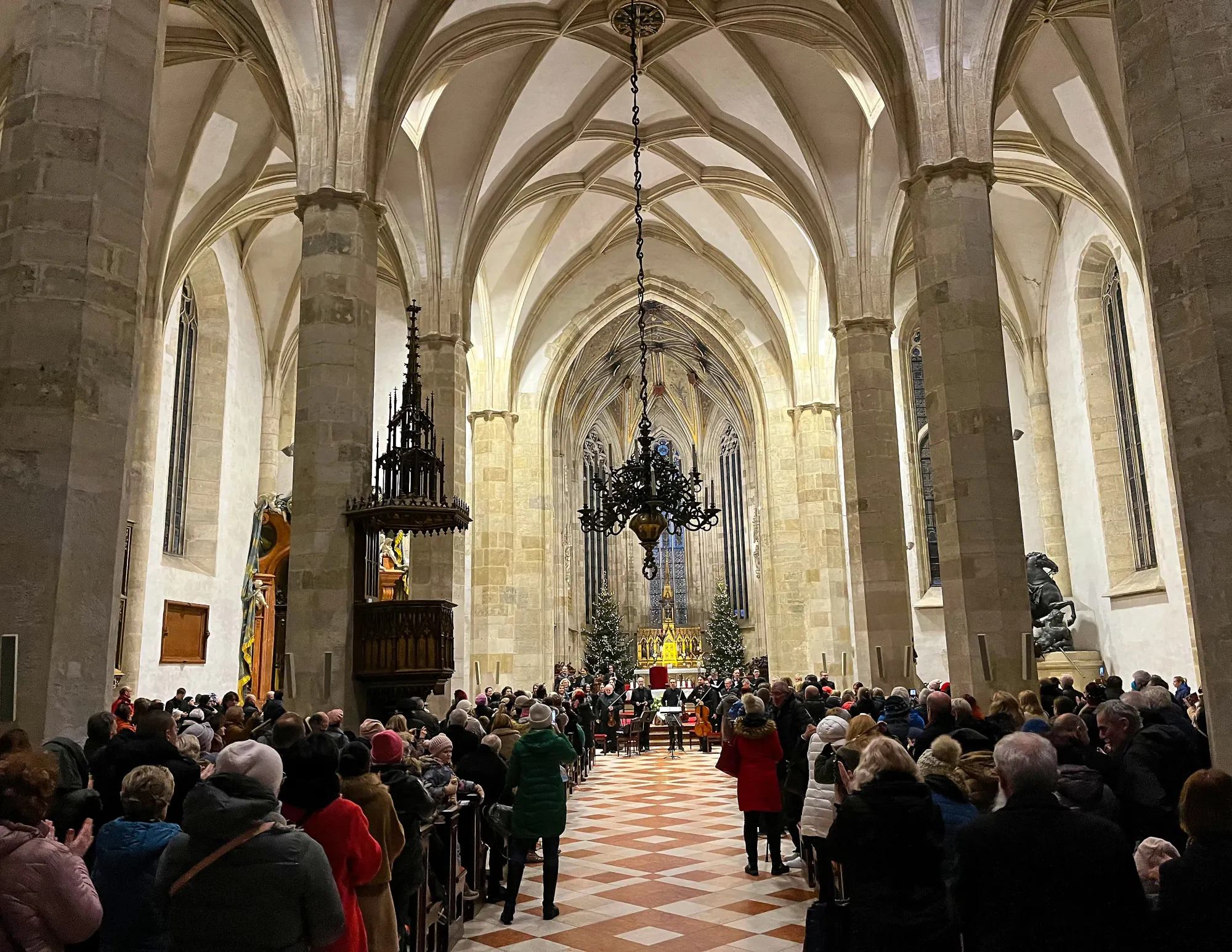 Arched church hall with stone flooring and packed pews with a choir at the altar