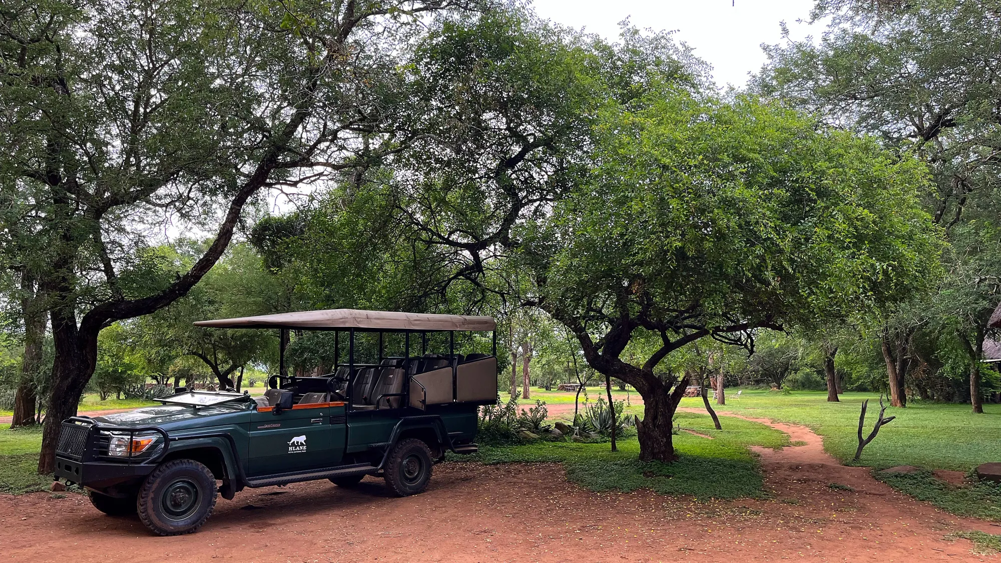 Green truck with a canvas awning sitting under trees