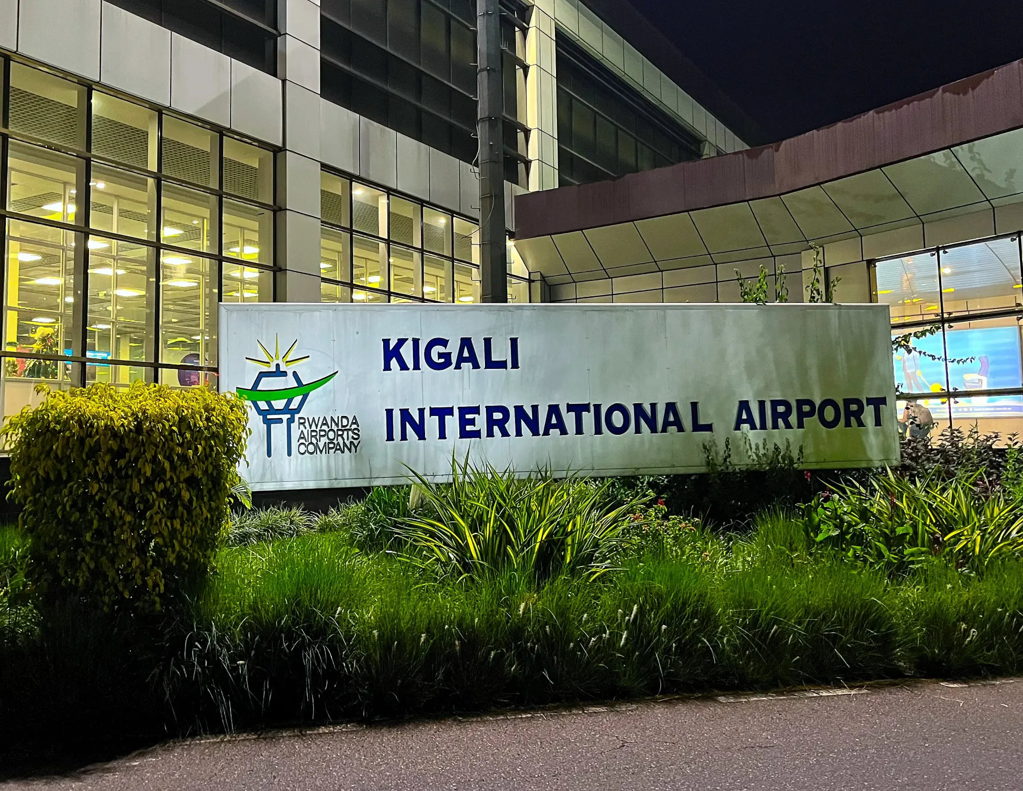 Sign for the airport surrounded by bushes with windows behind it