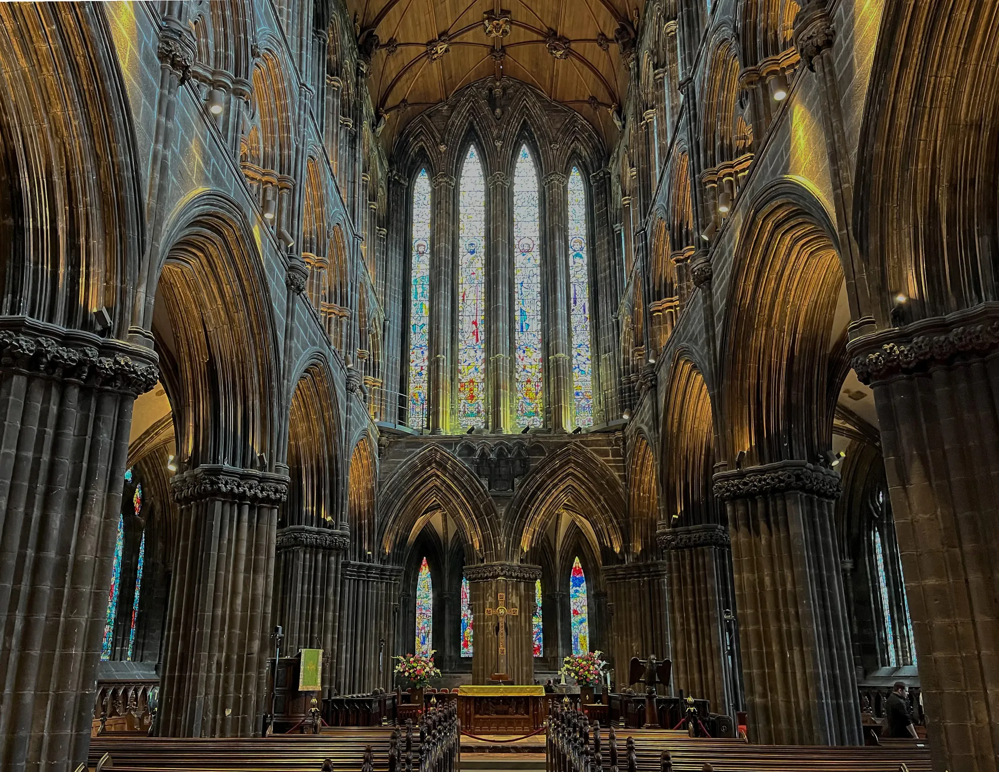 Dark church shot from the center aisle looking at the altar backed with stained glass