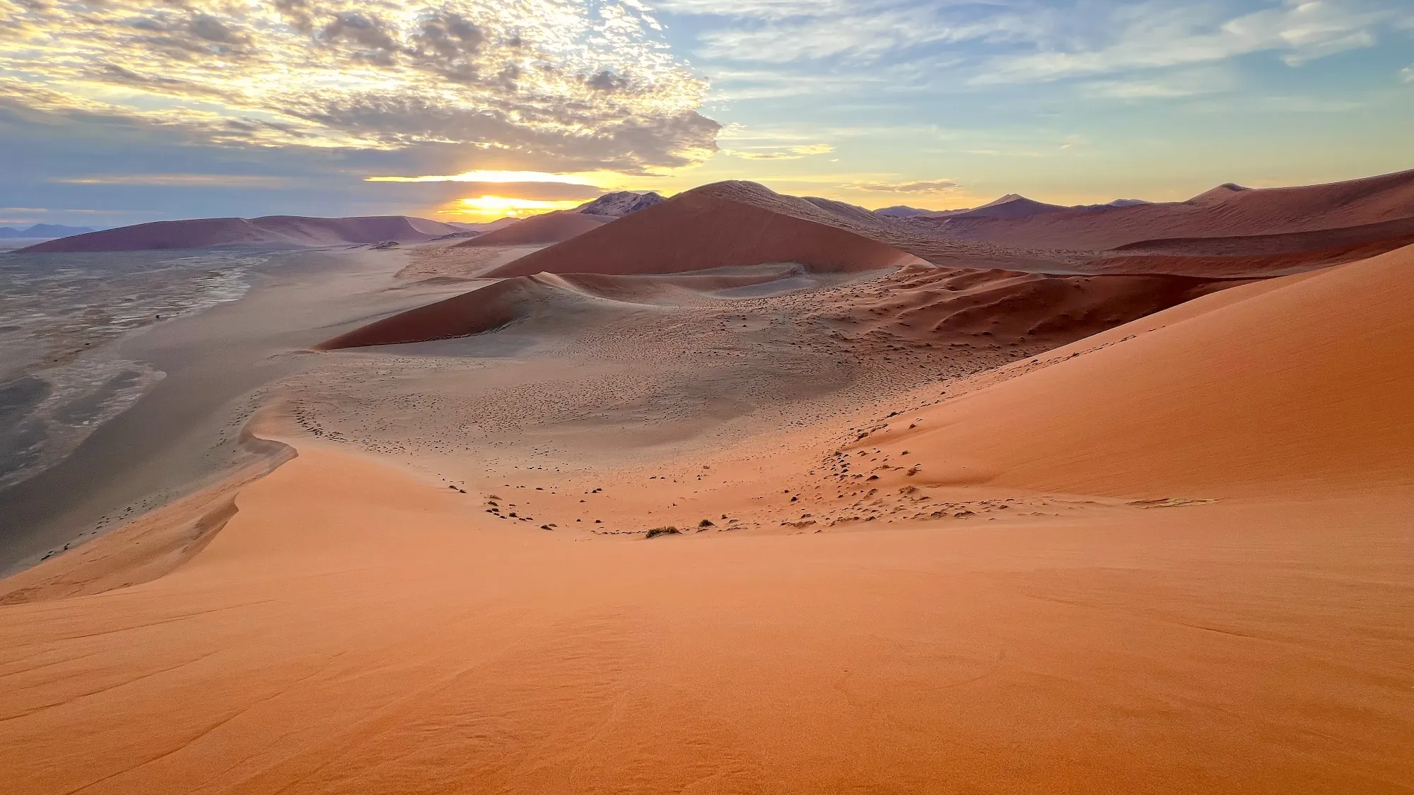 Soft dunes overlooking the sun break over the horizon above more dunes