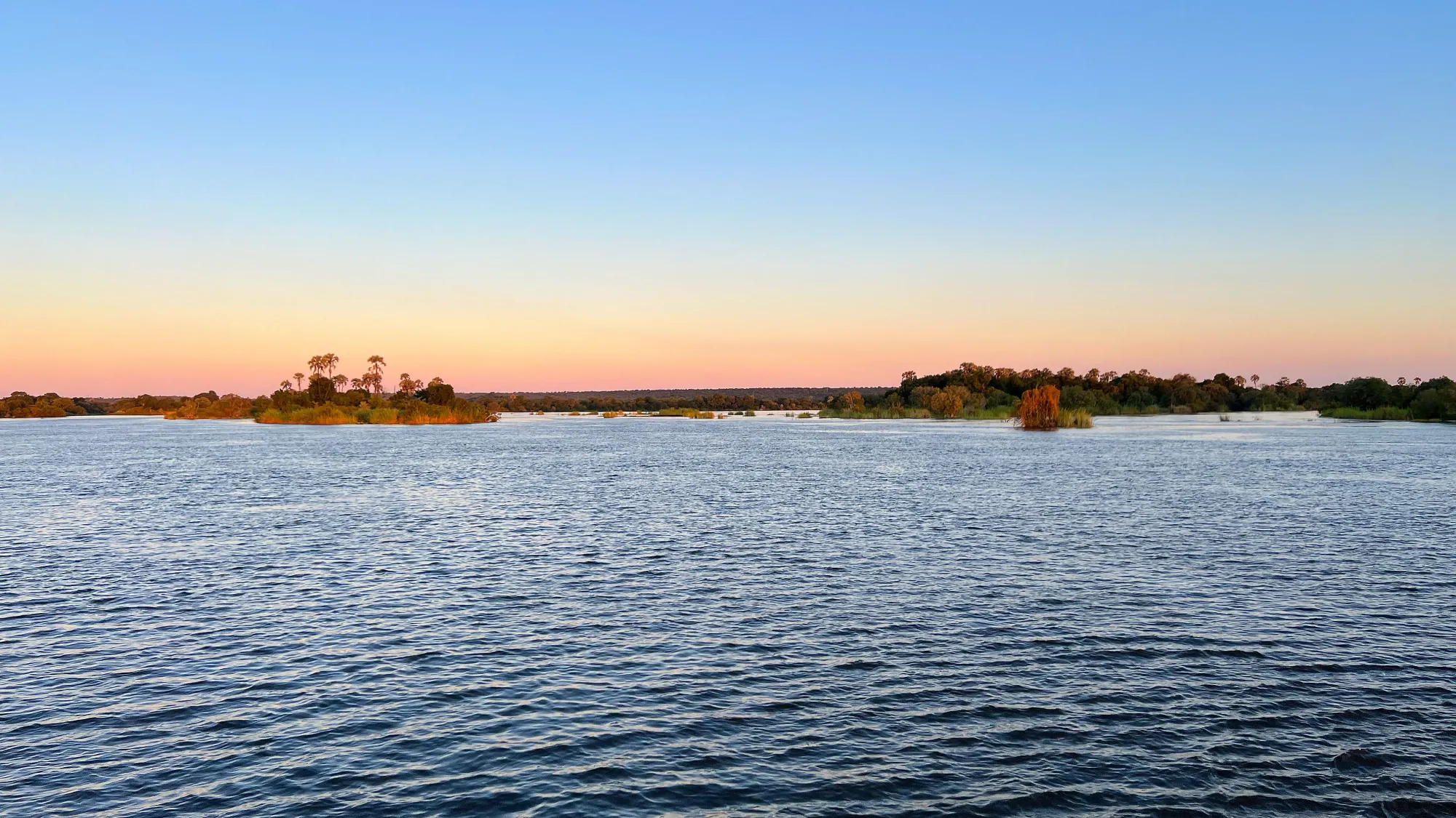 Blue river under and changing sky with small green islands floating in between