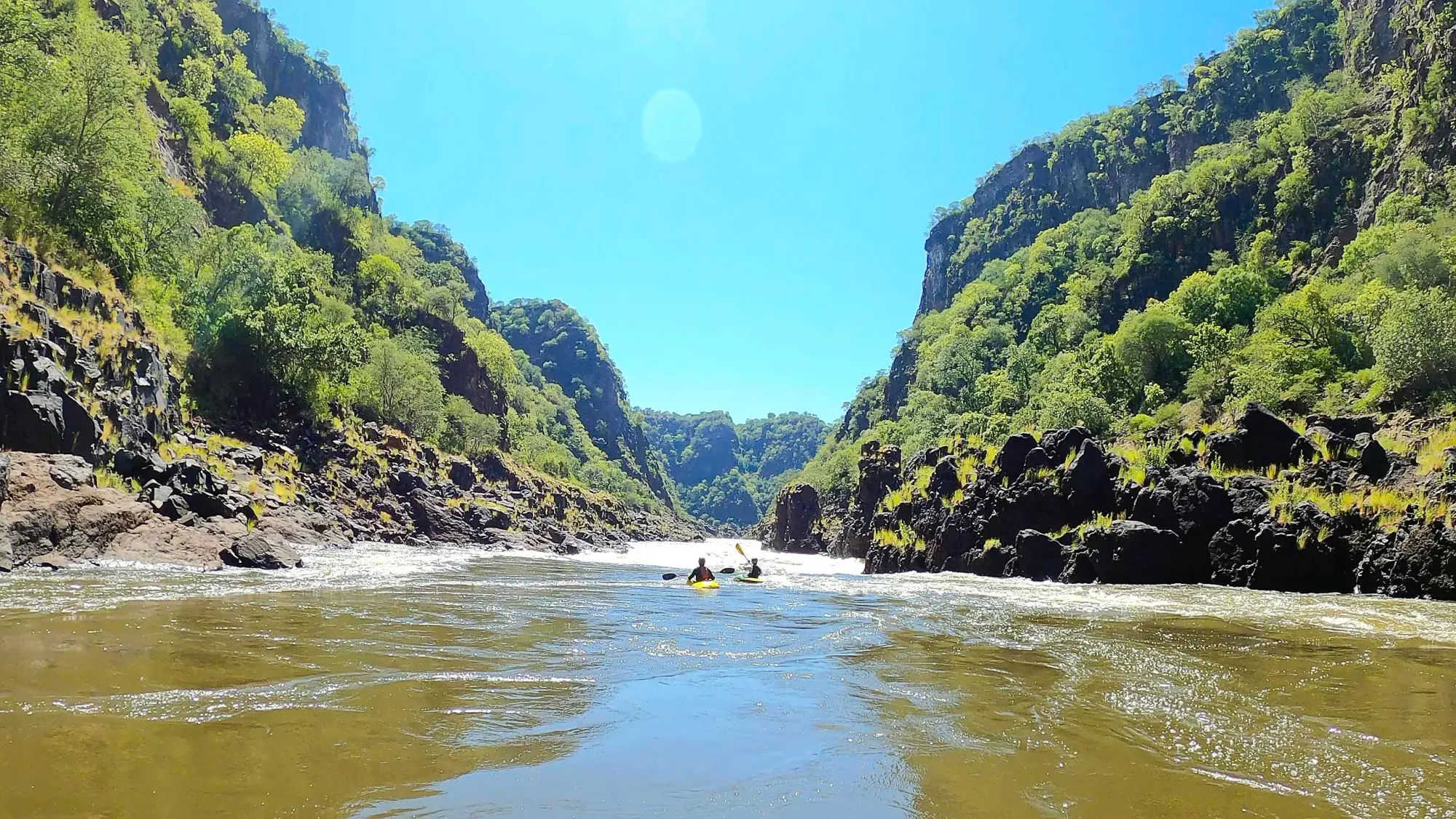 Flowing river wtih two kayakers and tall green hills rising out of either side