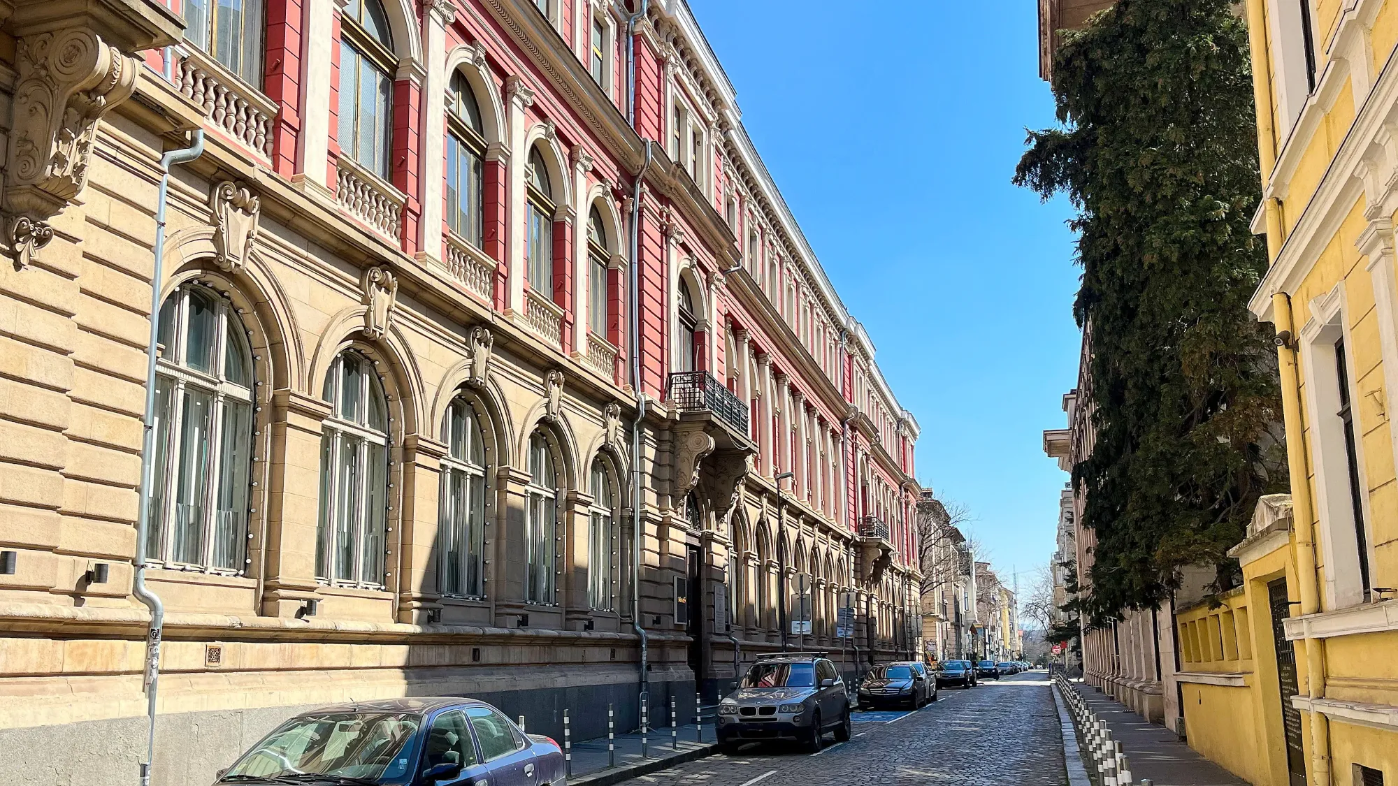 Stone streets with pastel buildings and a row of parked cars.