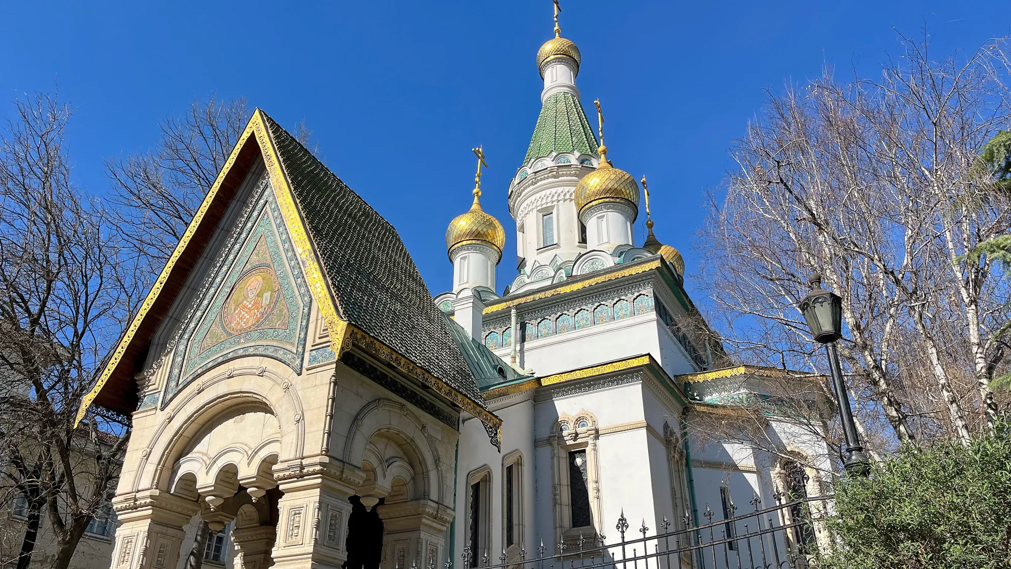 Pointy white church with green and gold shingles and detailing