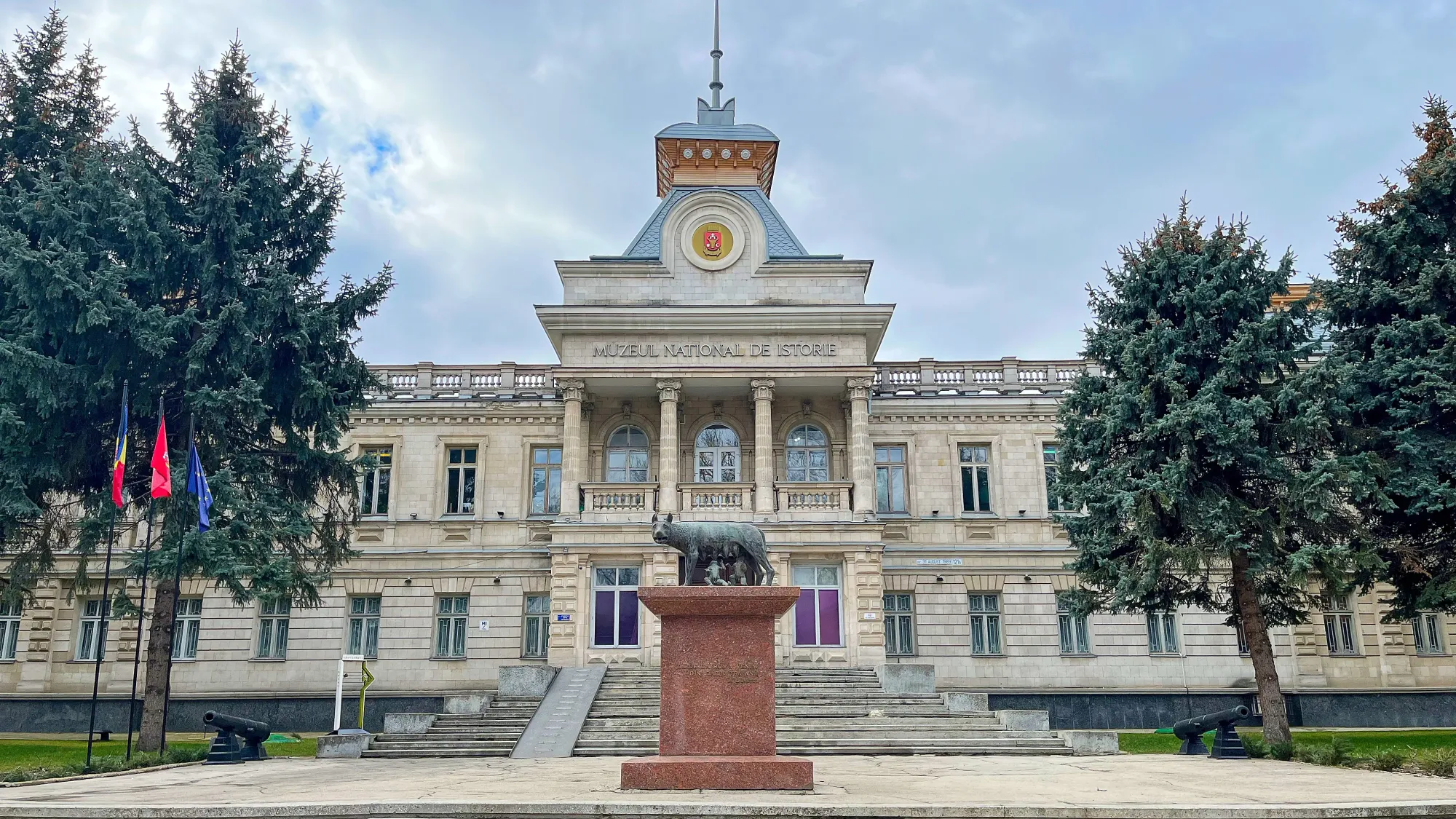 Stone building with four columns above the entry stairs and a statue of Romulus and Remus in front.