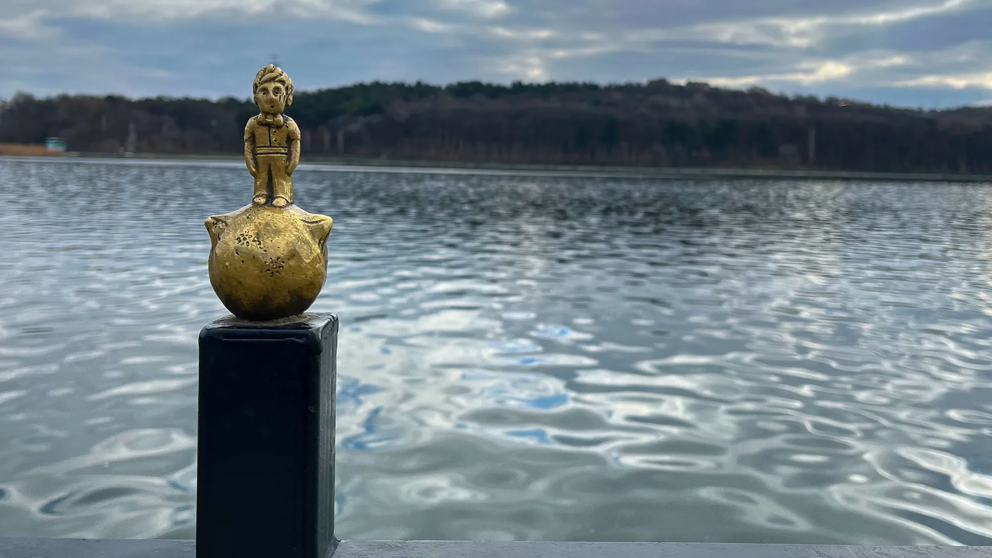 Golden mini-statue of The Little Prince in front of a lake