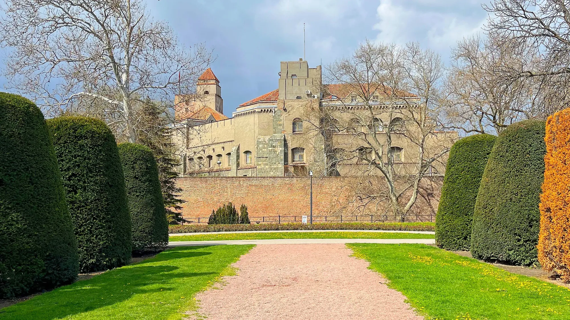 Stone fortress set behind a wall and framed with conical hedges