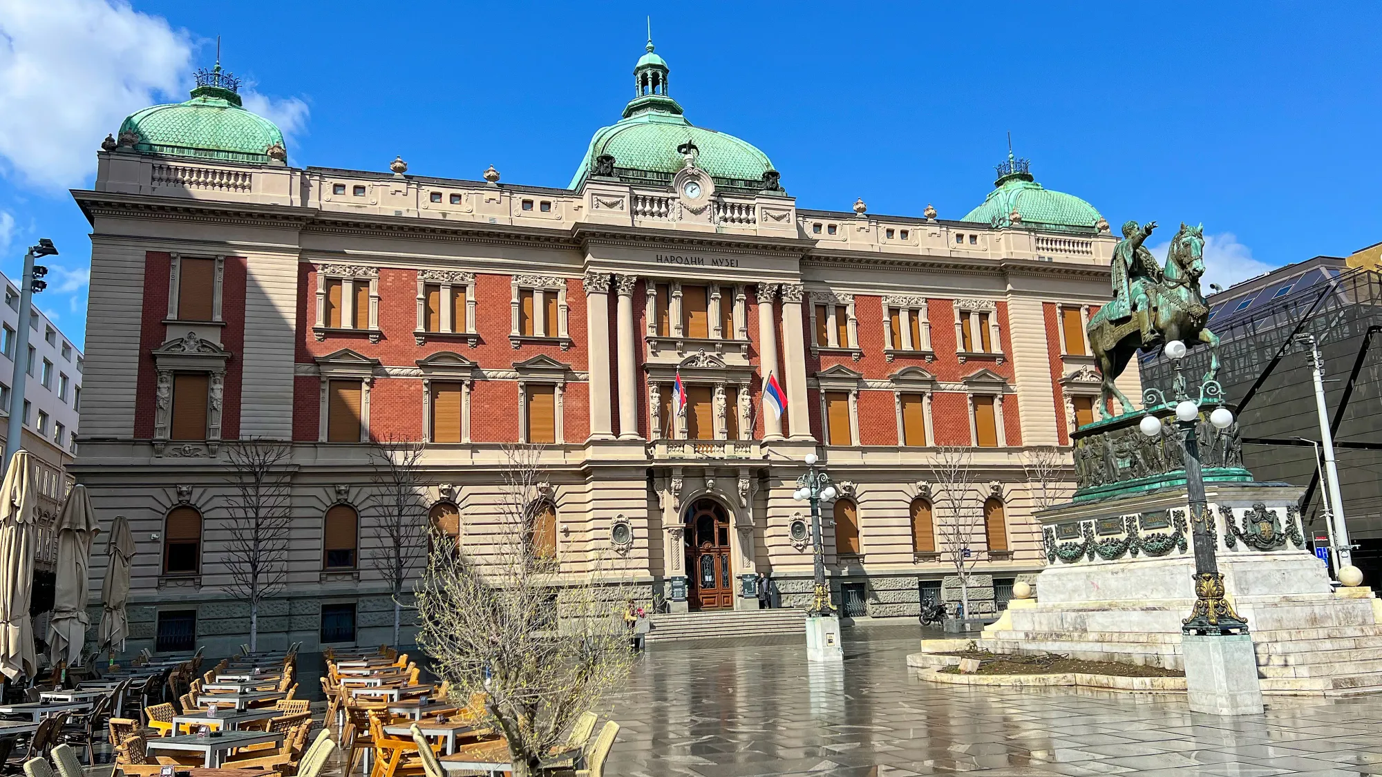 Building with green tiled roof and a statue of a man riding a horse in the center of the plaza