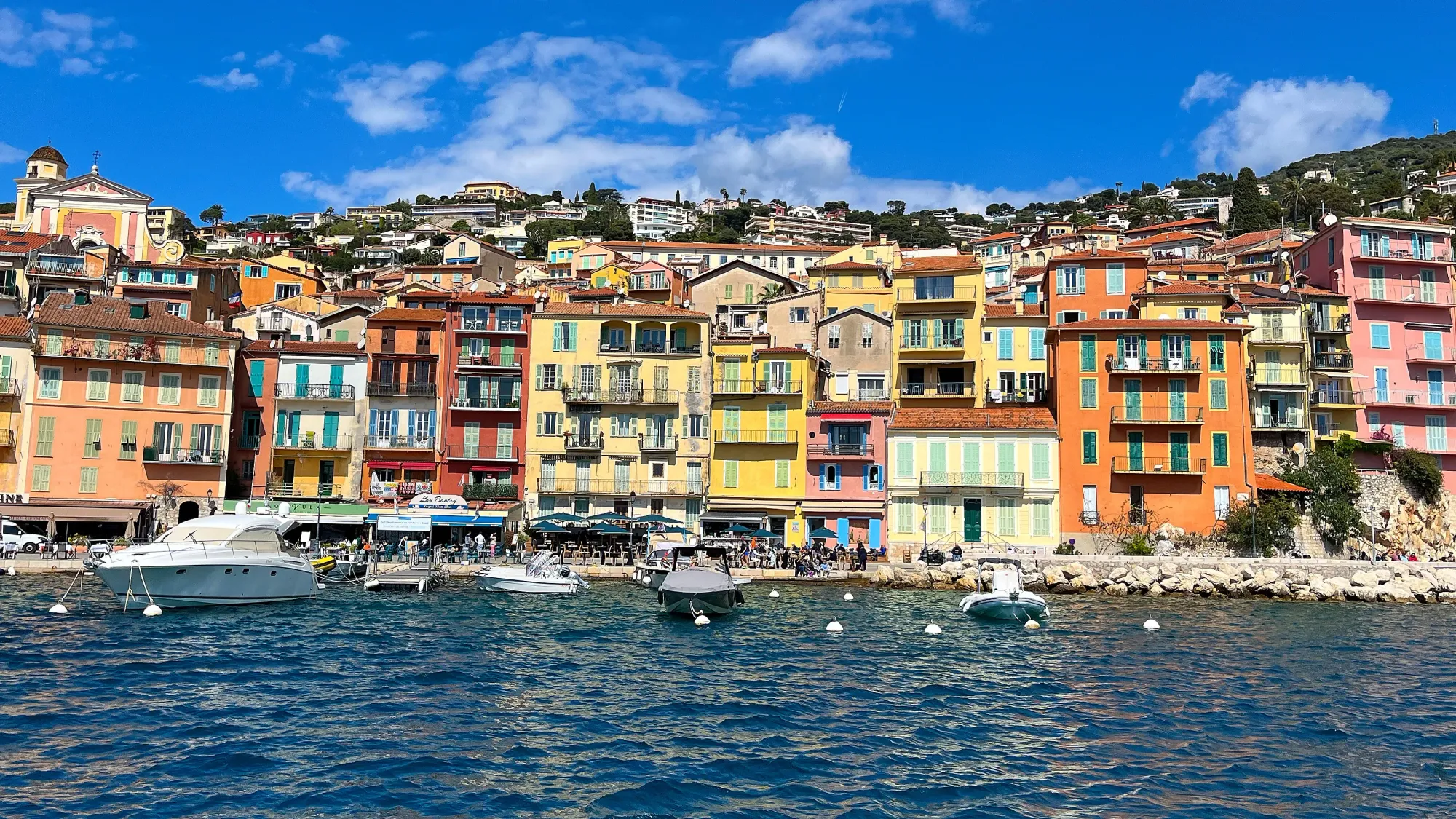 Orange, pink, and yellow buildings abutting the rocky coast lined with boats