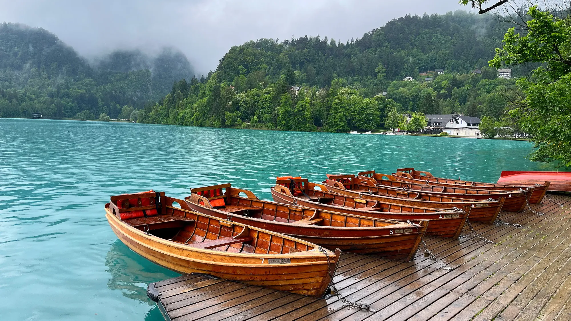 Six wooden boats docked against turquise water with greenery all around