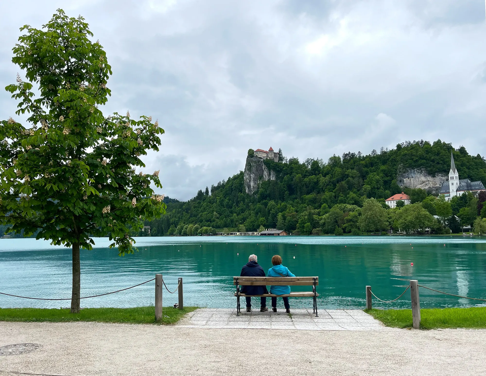 Two folks sitting on a bench looking out over the lake and the castle on the opposite shore