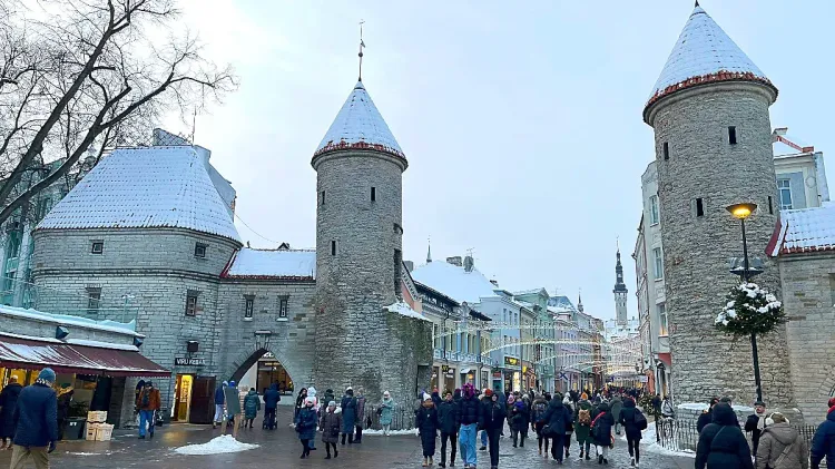 Snow-capped grey stone towers lining medieval street with lights and coat-wearing pedestrians