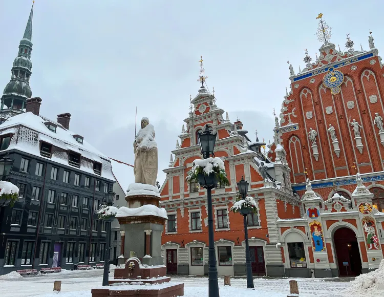 Snowy black and brick buildings with a medieval statue in the middle of the square