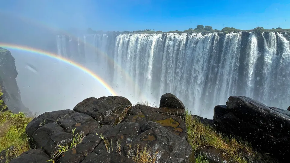 Rocks in the foreground and misty waterfalls in the background with a double rainbow on the left side